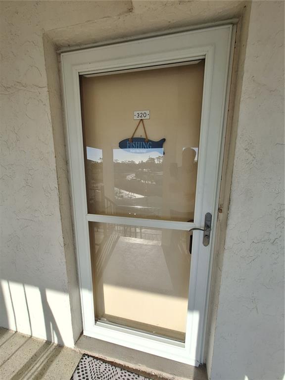 A white storm door with a fish-shaped sign labeled 320 is mounted on a stucco wall — 708 TAMIAMI TRAIL S UNIT 320, VENICE, FL