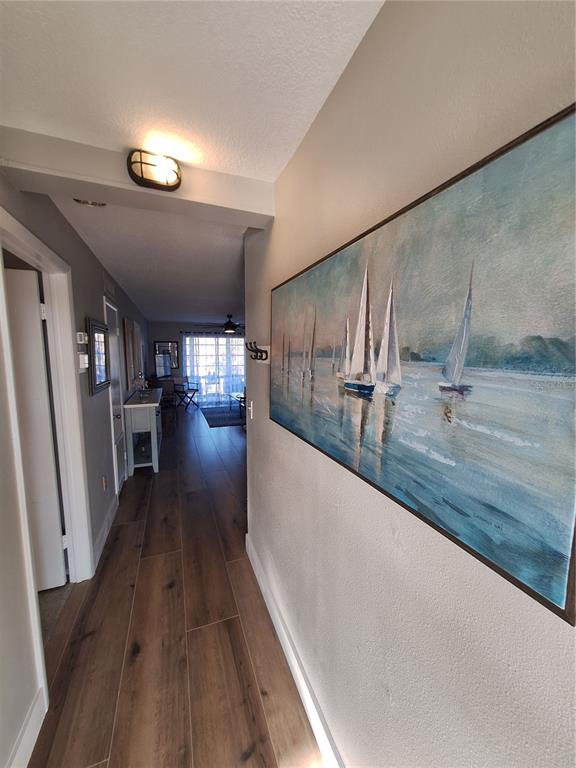A hallway with wood-look tile flooring leads to a living area, featuring a large sailboat painting — 708 TAMIAMI TRAIL S UNIT 320, VENICE, FL