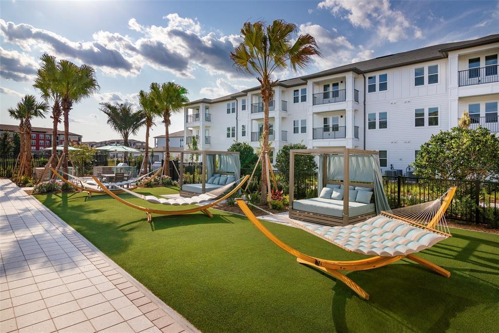 An outdoor lounge area features hammocks and cabanas on a lawn beside an apartment building — 100 WINDFLOWER LANE UNIT A1, DAYTONA BEACH, FL