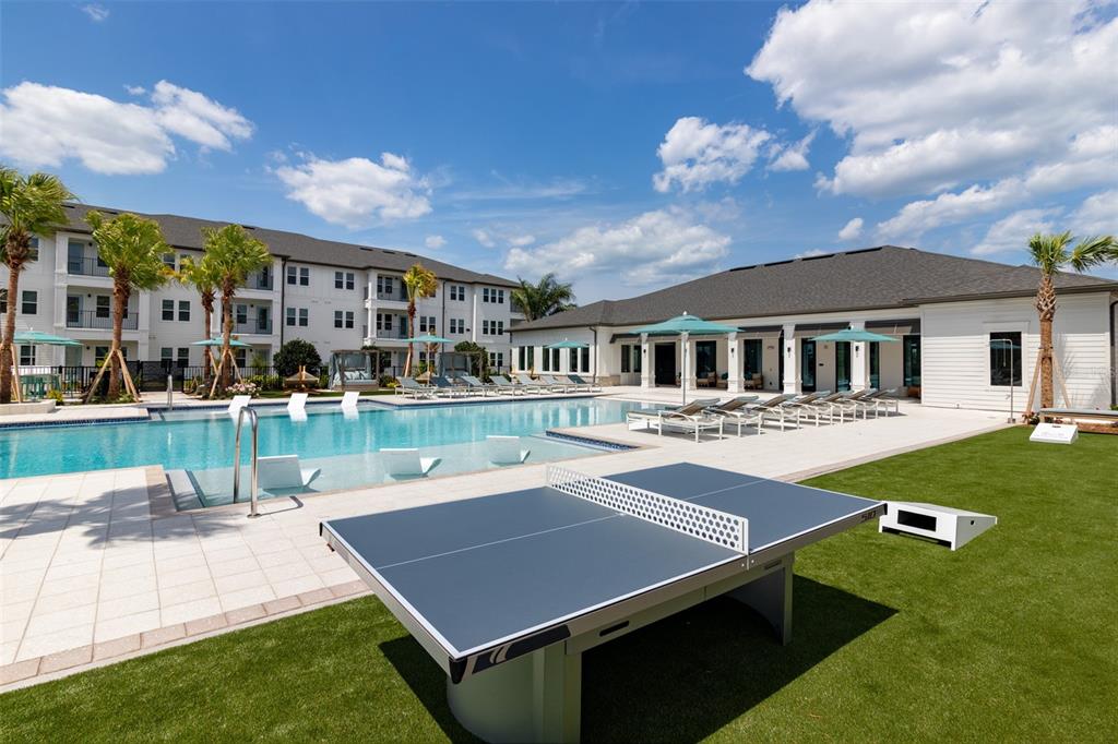 A ping pong table sits on a lawn beside a swimming pool and apartment building — 100 WINDFLOWER LANE UNIT A1, DAYTONA BEACH, FL