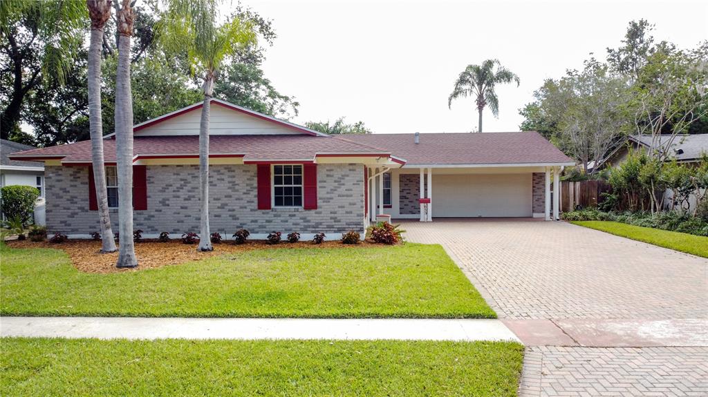 A single-story brick house features a red-trimmed roof, a paved driveway, and palm trees — 653 GREEN MEADOW AVENUE, MAITLAND, FL