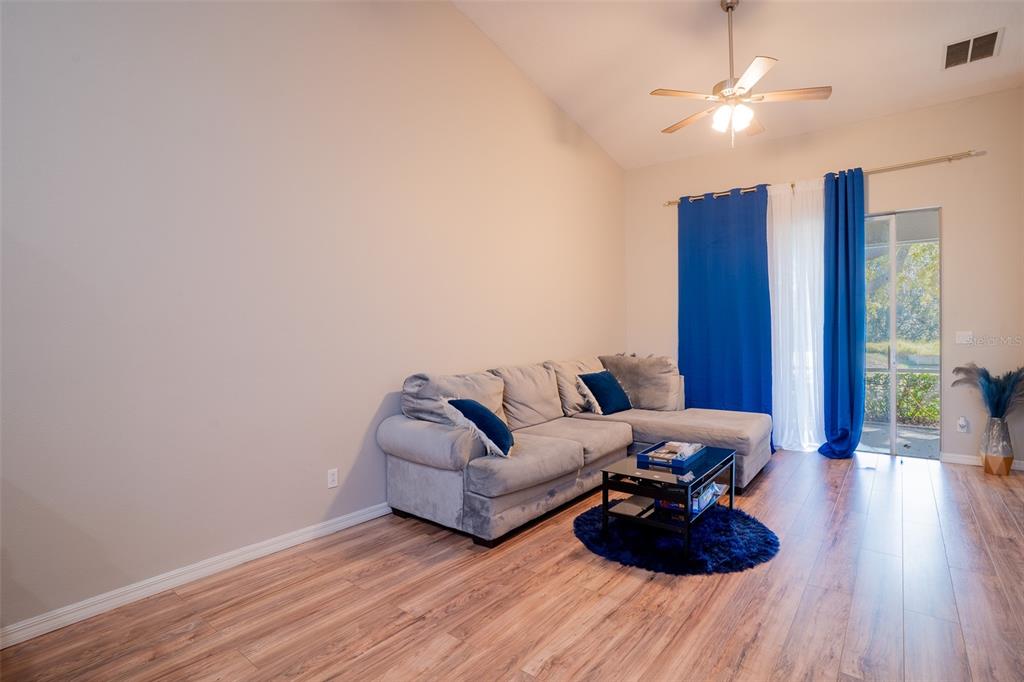 A living room features light walls, wood-look flooring, a gray sectional sofa, and blue curtains — 2739 RUTLEDGE COURT, WINTER HAVEN, FL