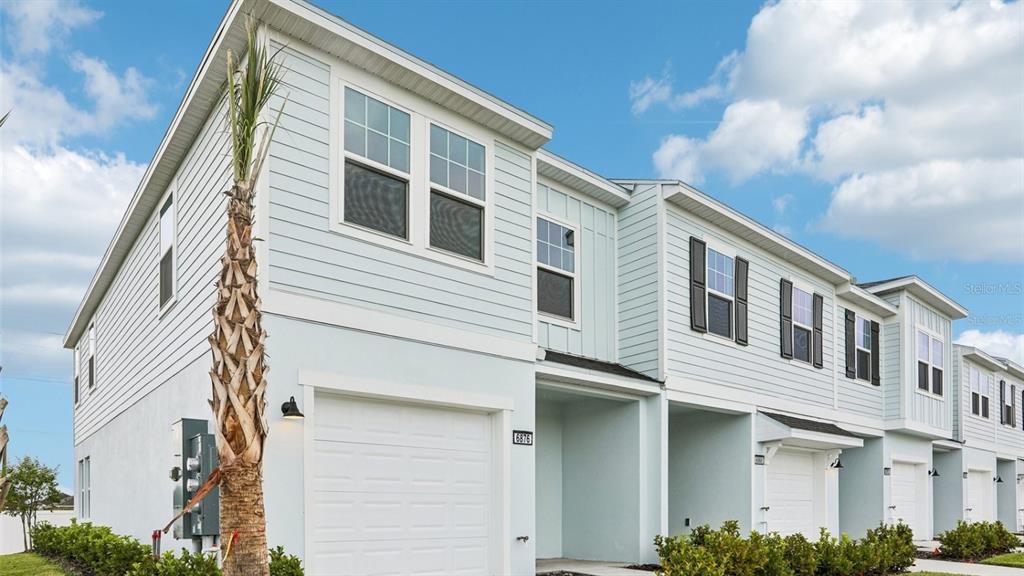 A row of light blue two-story townhomes with white garage doors and palm trees — 6876 HOLCOMBE DOWN DRIVE, ZEPHYRHILLS, FL