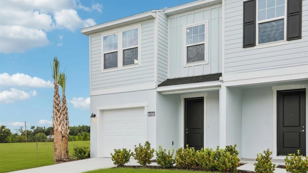 A two-story townhouse exterior with light blue siding, a single-car garage, and black doors — 6876 HOLCOMBE DOWN DRIVE, ZEPHYRHILLS, FL