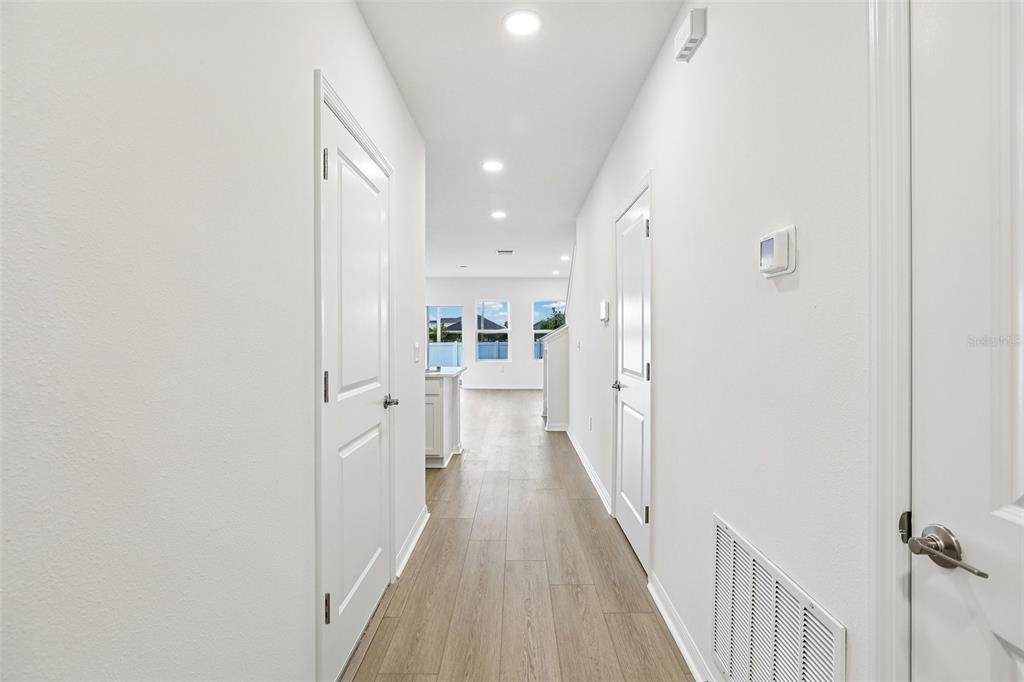 A bright hallway with light wood-look flooring leads toward an open-concept living area — 6876 HOLCOMBE DOWN DRIVE, ZEPHYRHILLS, FL