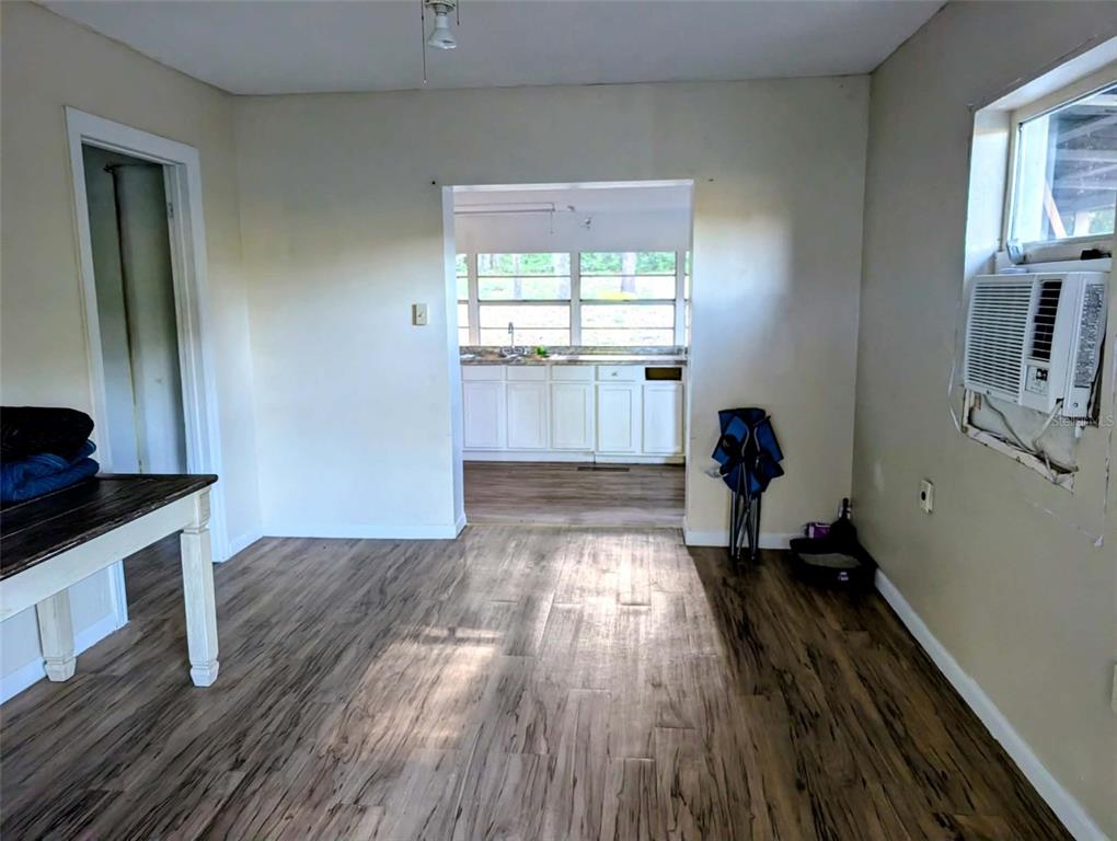 A room with wood-look flooring leads to a kitchen with white cabinets and windows — 17247 SE 284TH TERRACE, UMATILLA, FL