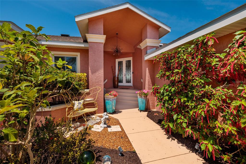 The front entrance of a peach-colored house features a walkway, potted flowers, and landscaping — 742 MONTE CRISTO BOULEVARD, TIERRA VERDE, FL