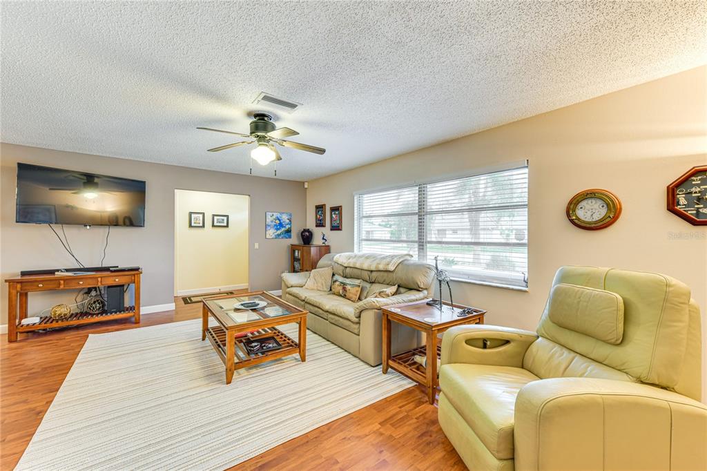 A living room with wood-look flooring, a ceiling fan, a sofa, and a recliner — 5008 MEDALIST ROAD, SARASOTA, FL