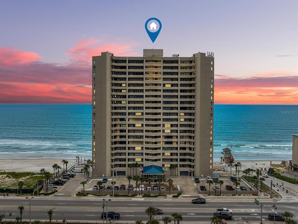An aerial view shows a coastal town with a bridge, buildings, and a sunset sky — 3425 S ATLANTIC AVENUE UNIT 1105, DAYTONA BEACH SHORES, FL