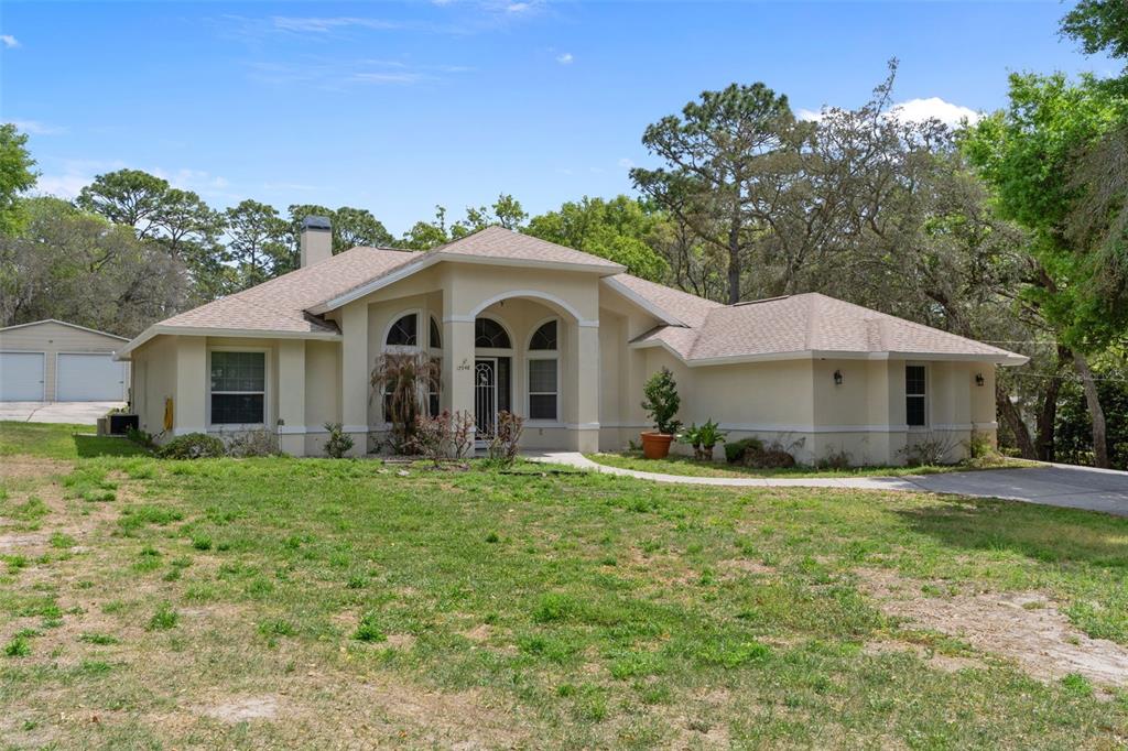 A single-story tan house with a hip roof and a detached garage sits on a lawn — 17948 GREENSBORO STREET, SPRING HILL, FL