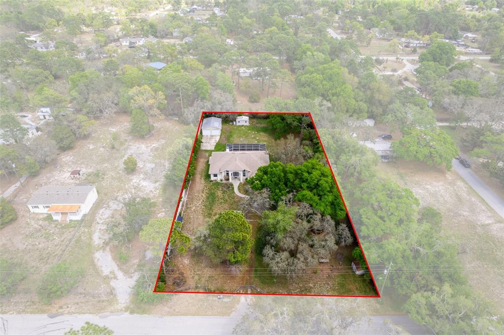 An aerial view shows a house with a pool enclosure on a large, wooded lot — 17948 GREENSBORO STREET, SPRING HILL, FL