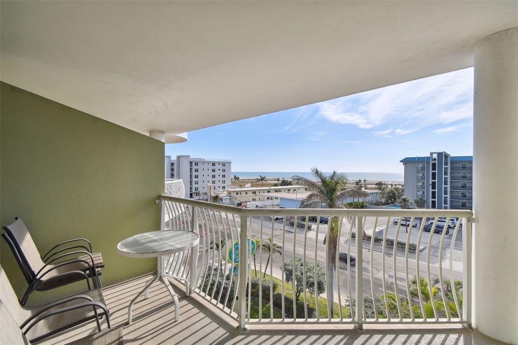 A balcony with two chairs and a small table overlooks a street and the ocean — 11605 GULF BOULEVARD UNIT 502, TREASURE ISLAND, FL