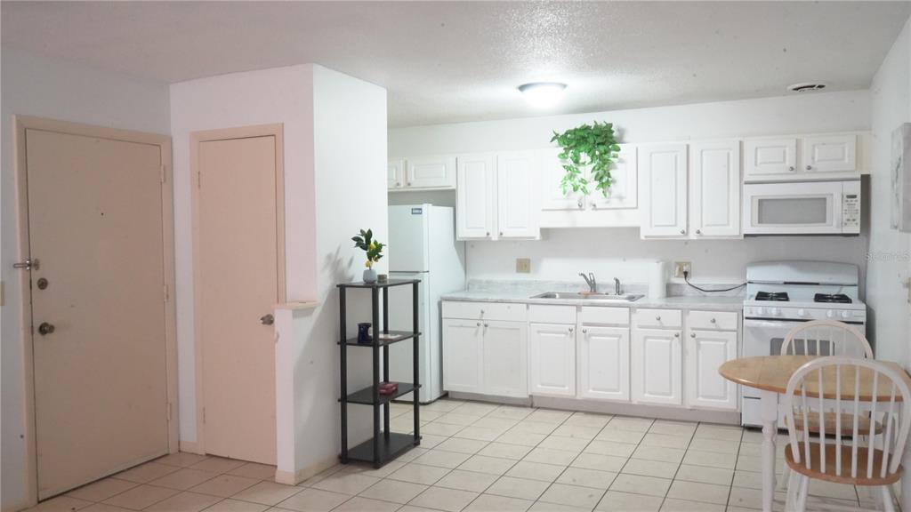 A kitchen features white cabinets, white appliances, a tiled floor, and a small dining table — 1700 SW 16TH COURT UNIT J-4, GAINESVILLE, FL