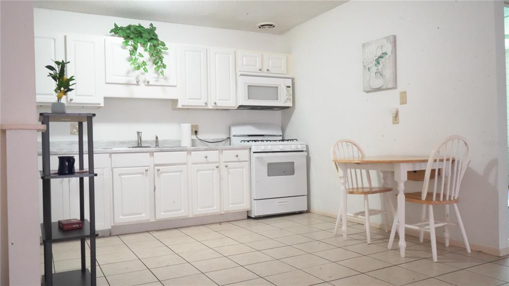 A kitchen with white cabinets, white appliances, a small dining table, and tiled flooring — 1700 SW 16TH COURT UNIT J-4, GAINESVILLE, FL