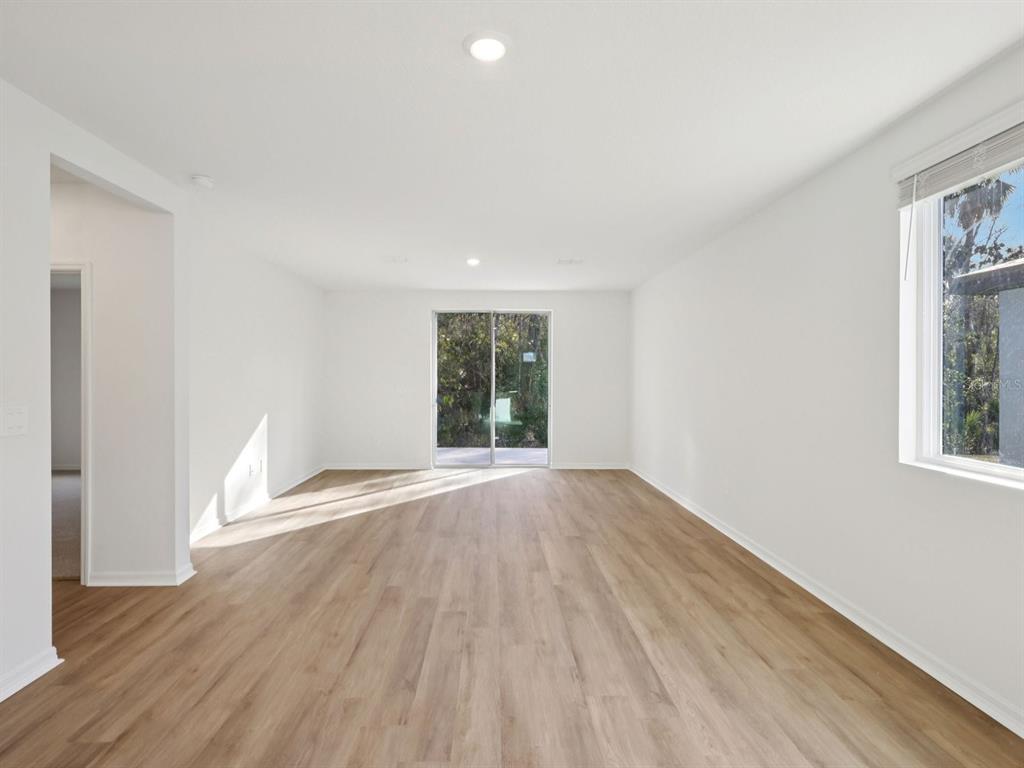 An empty living room with white walls, light wood-look flooring, and a sliding glass door — 13518 SHELLMORE AVENUE, PALMETTO, FL