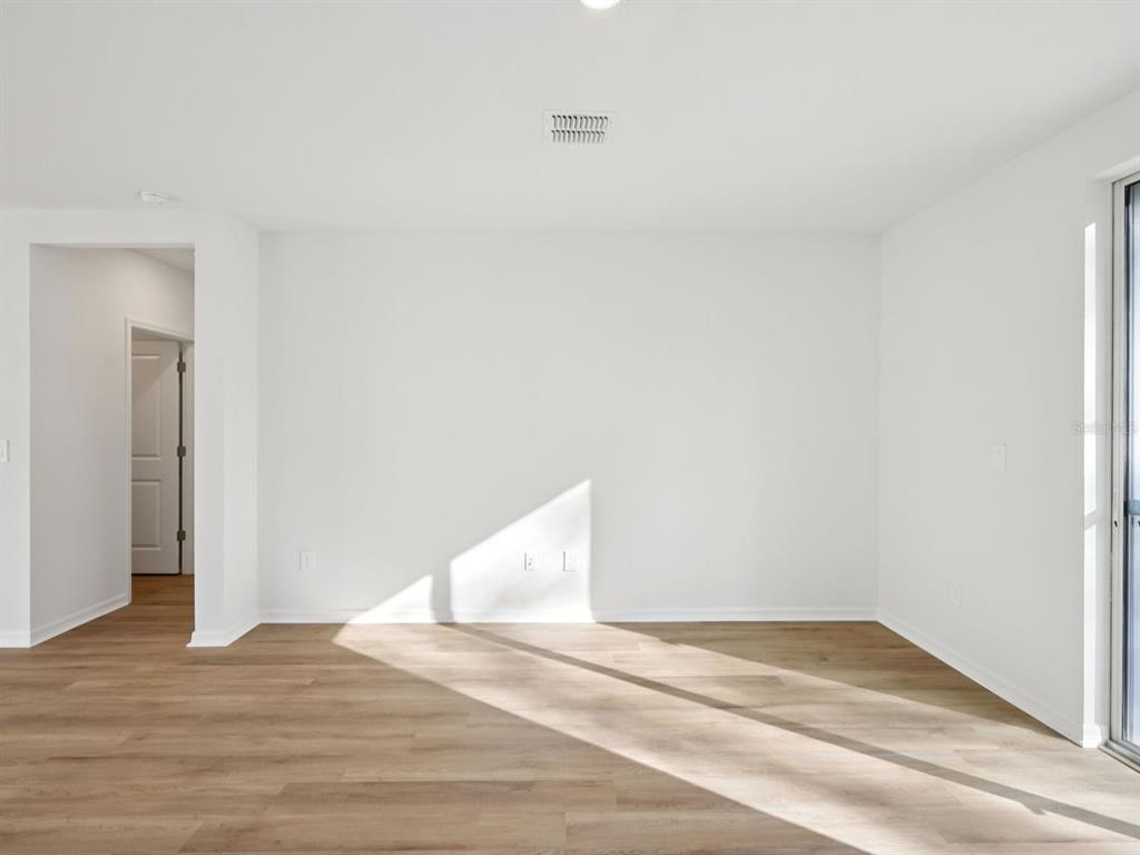 An empty room with white walls, light wood-look flooring, and a sliding glass door — 13518 SHELLMORE AVENUE, PALMETTO, FL