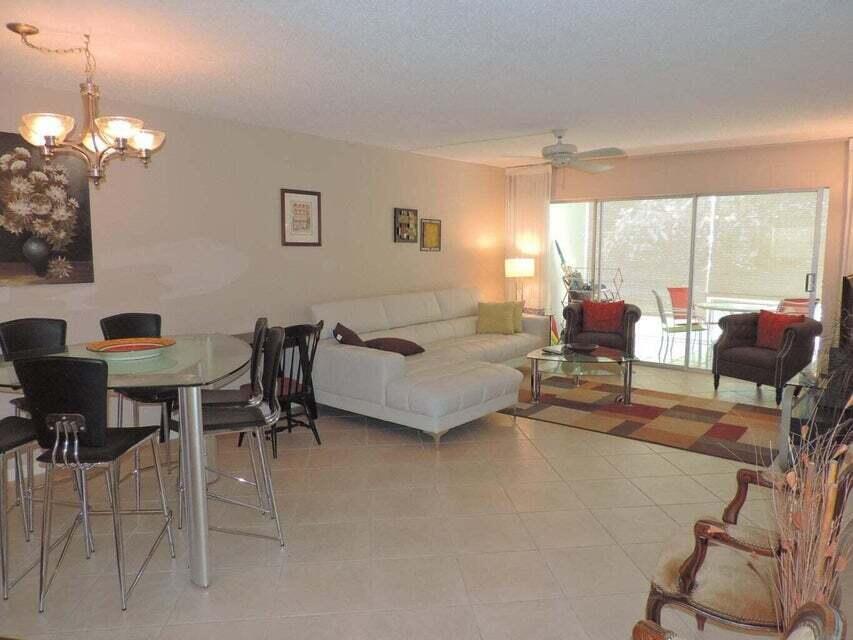 A living and dining area with tile floors, a white sectional sofa, and glass doors — 20 Celestial Way # 105, Juno Beach FL 33408, JUNO BEACH, FL