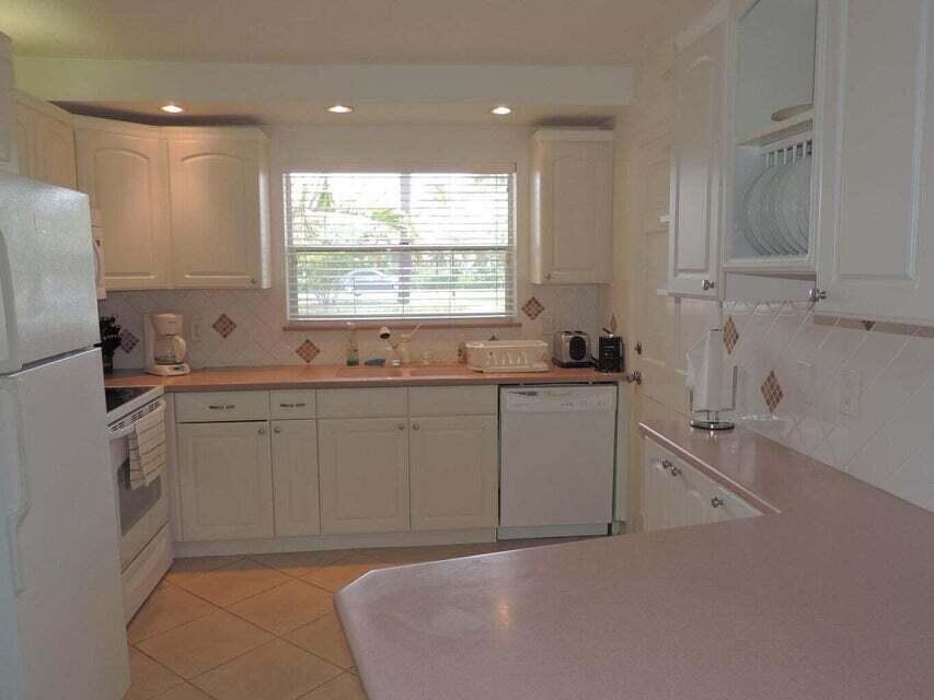 A kitchen features white cabinetry, pink countertops, a white dishwasher, and a window over the sink — 20 Celestial Way # 105, Juno Beach FL 33408, JUNO BEACH, FL