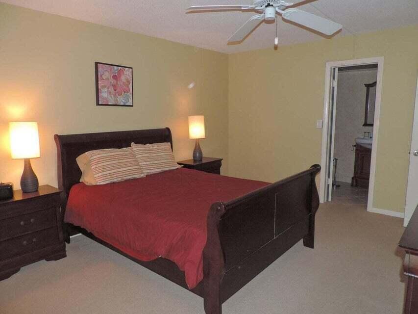A bedroom with a dark wood sleigh bed, two matching nightstands, and an attached bathroom — 20 Celestial Way # 105, Juno Beach FL 33408, JUNO BEACH, FL