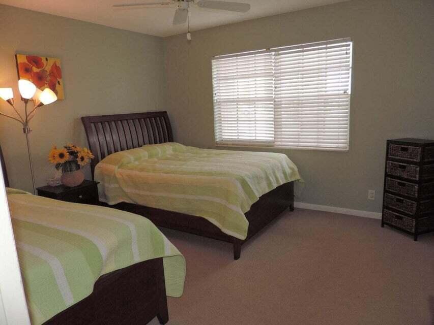 A bedroom features two beds with green striped bedding, a floor lamp, and a dresser — 20 Celestial Way # 105, Juno Beach FL 33408, JUNO BEACH, FL