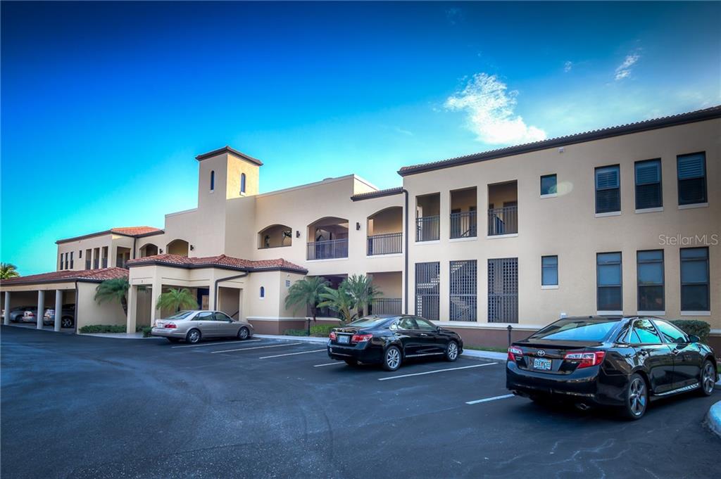 A multi-story apartment building with a parking lot and several parked cars in front — 3334 PURPLE MARTIN DRIVE UNIT 211, PUNTA GORDA, FL