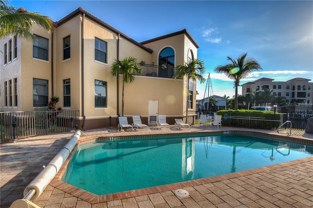 A swimming pool sits on a paved patio beside a multi-story tan stucco building — 3334 PURPLE MARTIN DRIVE UNIT 211, PUNTA GORDA, FL