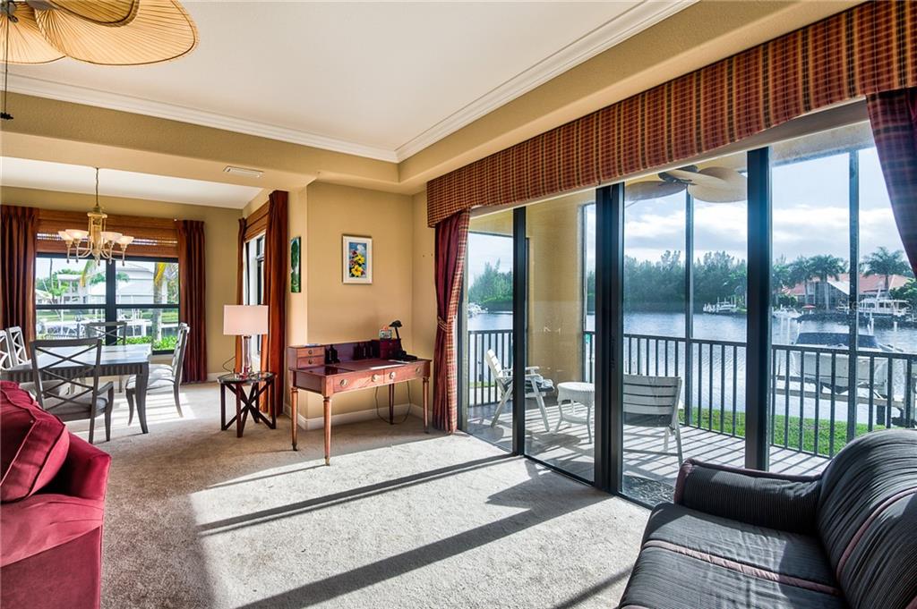 A living room with a desk, dining area, and sliding glass doors overlooking a canal — 3334 PURPLE MARTIN DRIVE UNIT 211, PUNTA GORDA, FL