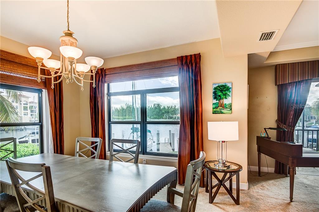 A dining room with a wooden table, chandelier, and large windows overlooking a marina — 3334 PURPLE MARTIN DRIVE UNIT 211, PUNTA GORDA, FL