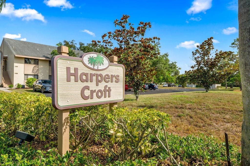 A sign for Harpers Croft stands in front of a residential building and trees — 5146 HARPERS CROFT UNIT 13, SARASOTA, FL