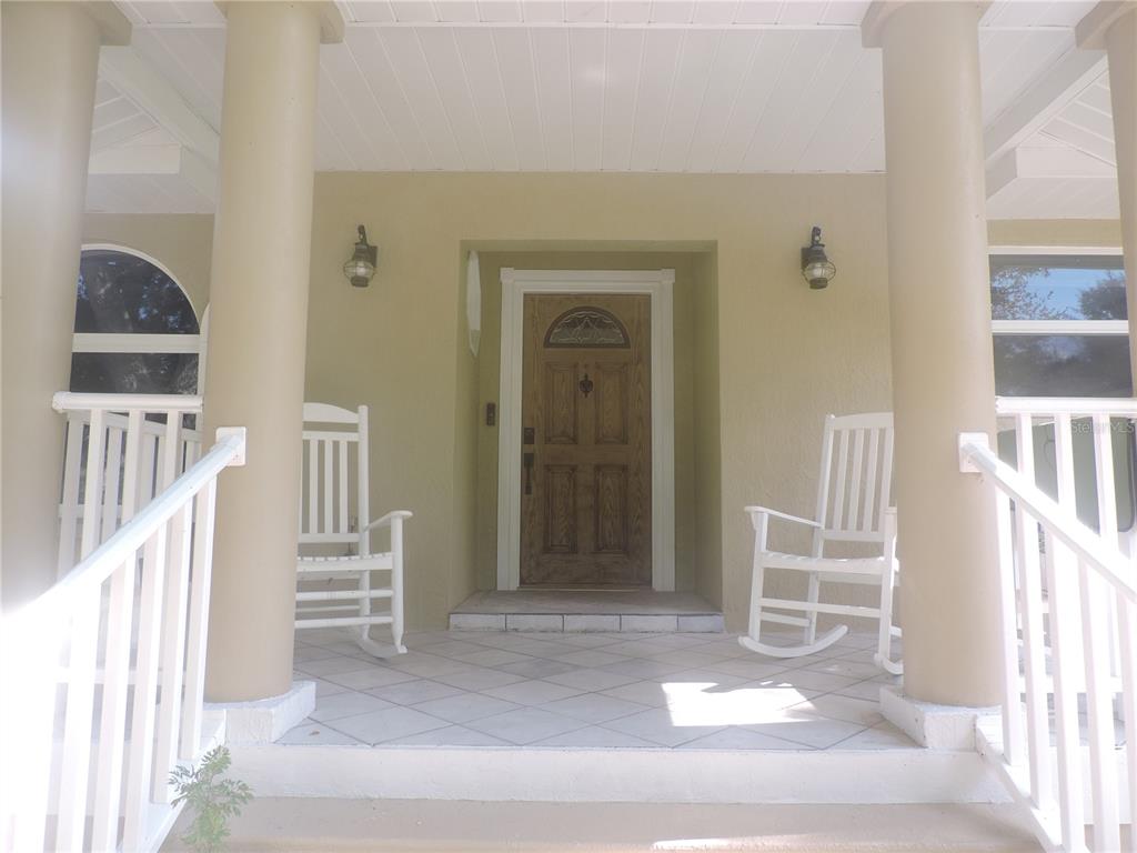A covered front porch features two white rocking chairs, tiled flooring, and a wooden door — 905 COLONIAL ROAD, VENICE, FL