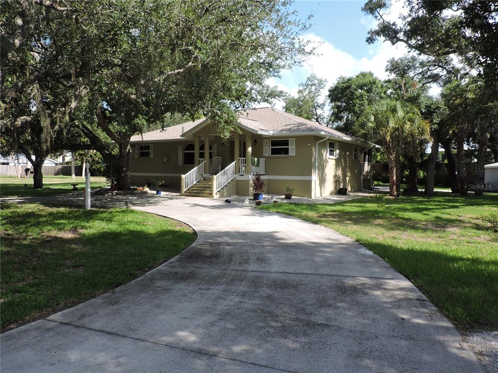 A single-story house with a tan exterior and a concrete driveway sits among large trees — 905 COLONIAL ROAD, VENICE, FL