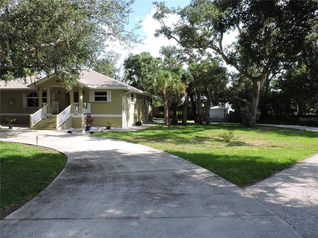 A light green house with a concrete driveway and large trees in the front yard — 905 COLONIAL ROAD, VENICE, FL