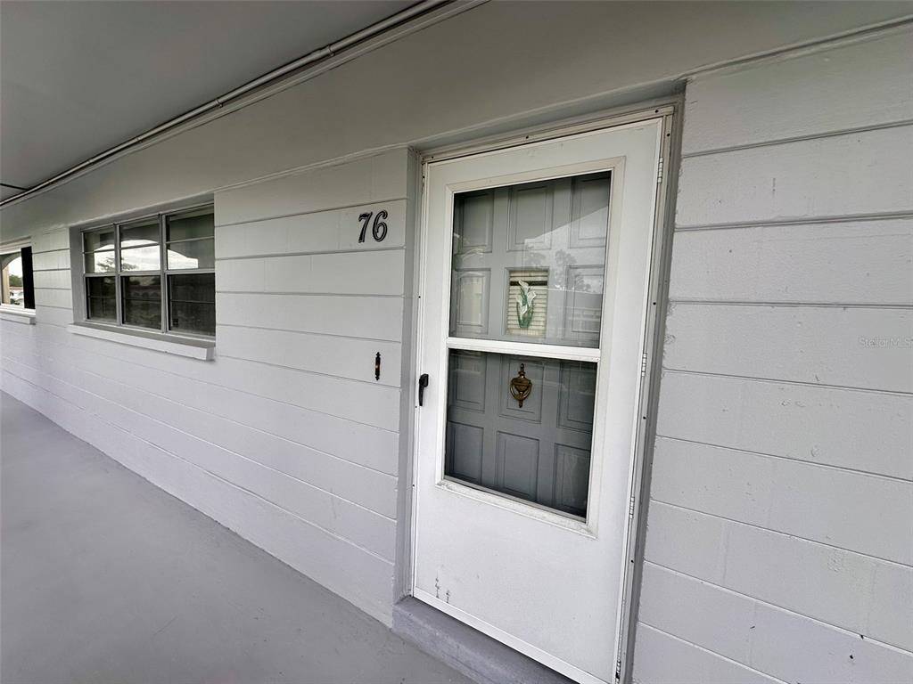 A white exterior wall features a numbered door and a window along a walkway — 2460 FRANCISCAN DRIVE UNIT 76, CLEARWATER, FL