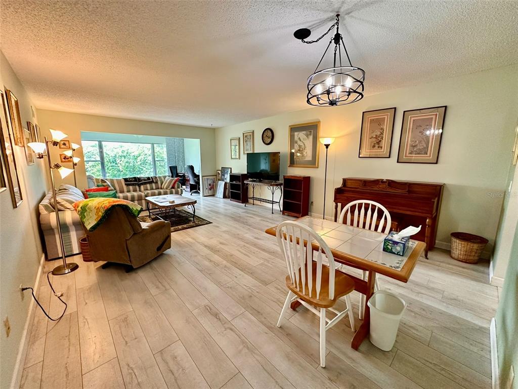 A living and dining area features light wood-look flooring, a chandelier, and a piano — 2460 FRANCISCAN DRIVE UNIT 76, CLEARWATER, FL