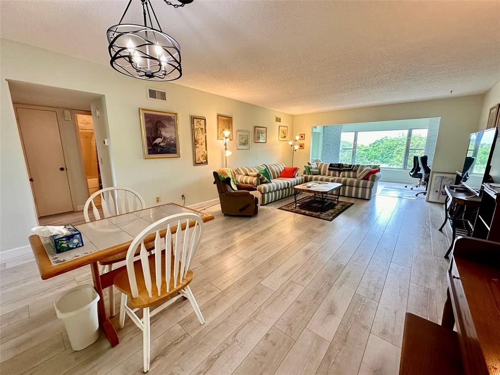 A living and dining room features light wood-look flooring, a striped sofa, and large windows — 2460 FRANCISCAN DRIVE UNIT 76, CLEARWATER, FL