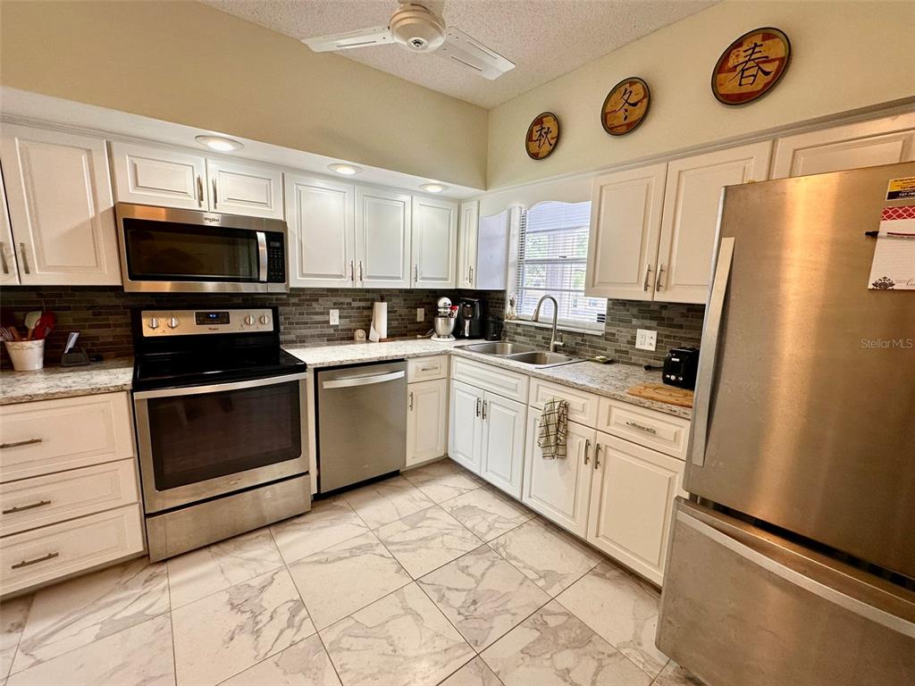 A kitchen features white cabinets, stainless steel appliances, granite countertops, and light-colored tile flooring — 2460 FRANCISCAN DRIVE UNIT 76, CLEARWATER, FL