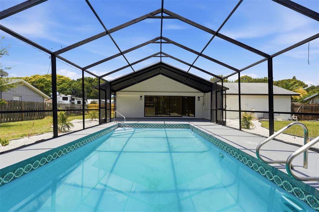 A swimming pool enclosed by a screened lanai sits behind a single-story residential home — 4731 ATLANTIC AVENUE, SARASOTA, FL