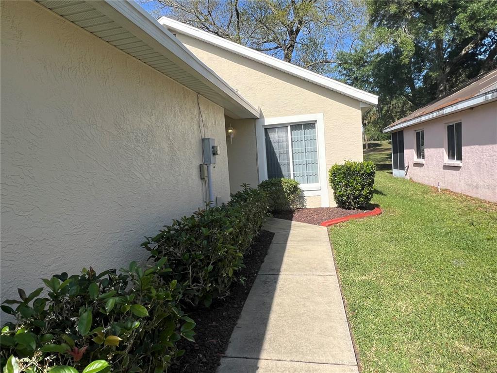 A concrete walkway leads to the entrance of a beige stucco house with a window — 1918 NW 50TH CIRCLE, OCALA, FL