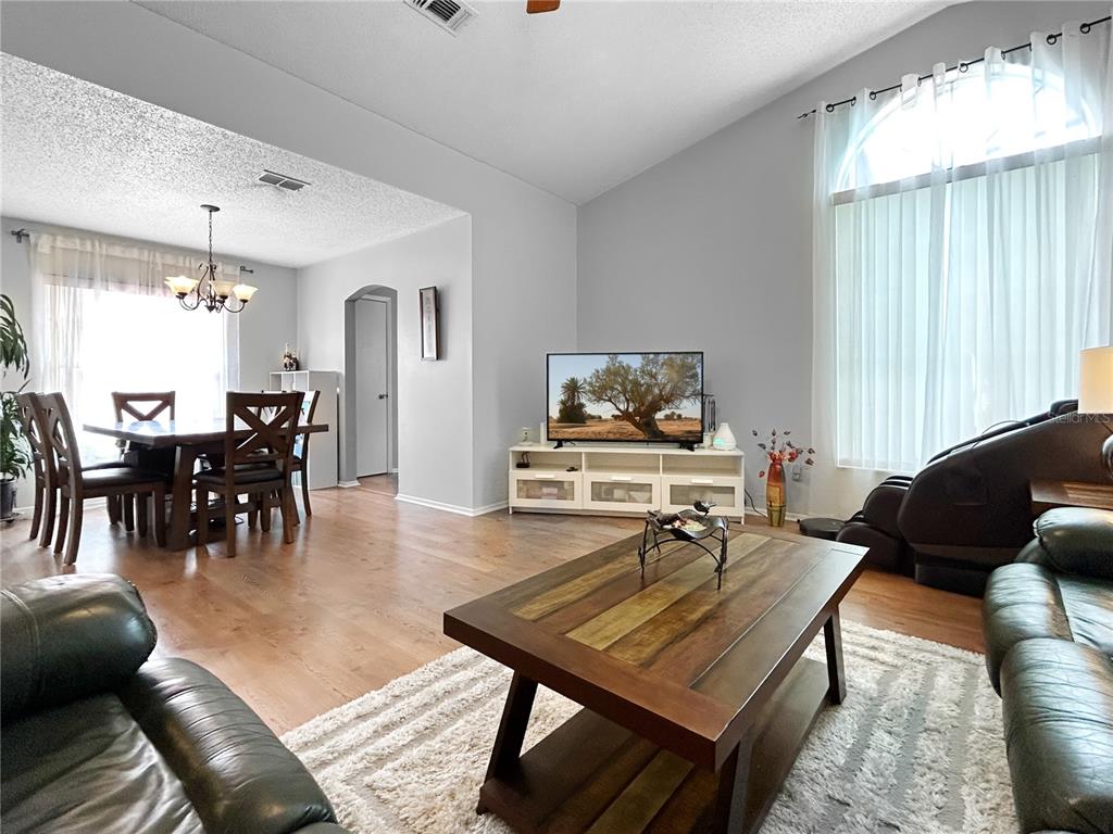 A living room with wood flooring, a coffee table, a television, and an adjacent dining area — 3228 RUNNING BEAR WAY, KISSIMMEE, FL