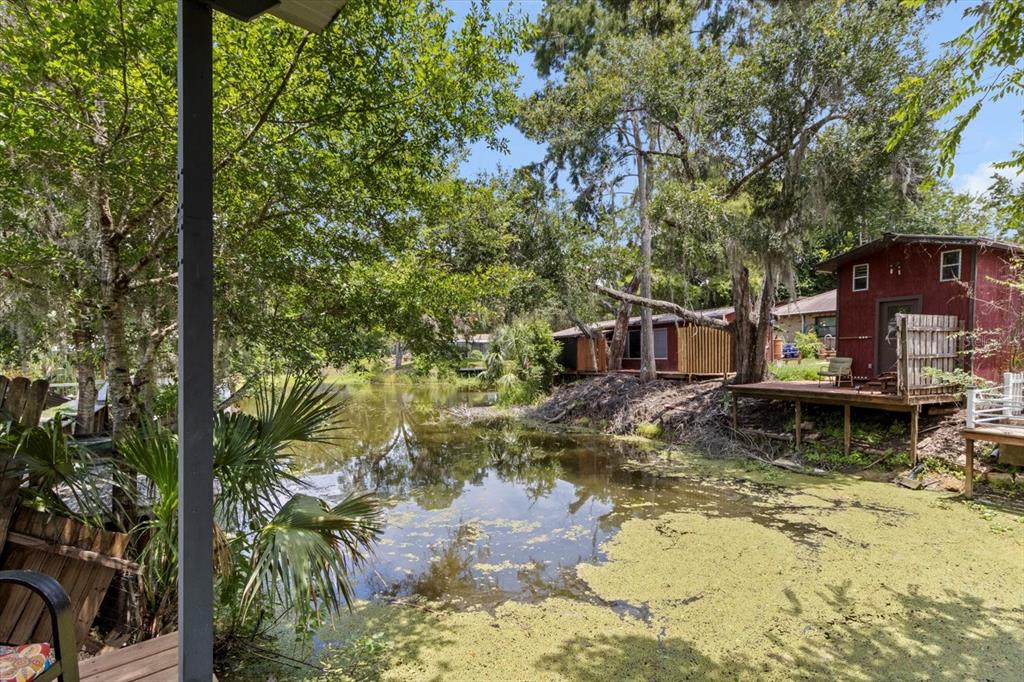 A red cabin with a wooden deck overlooks a pond covered in green algae — 609 S REDBUD TERRACE, INVERNESS, FL