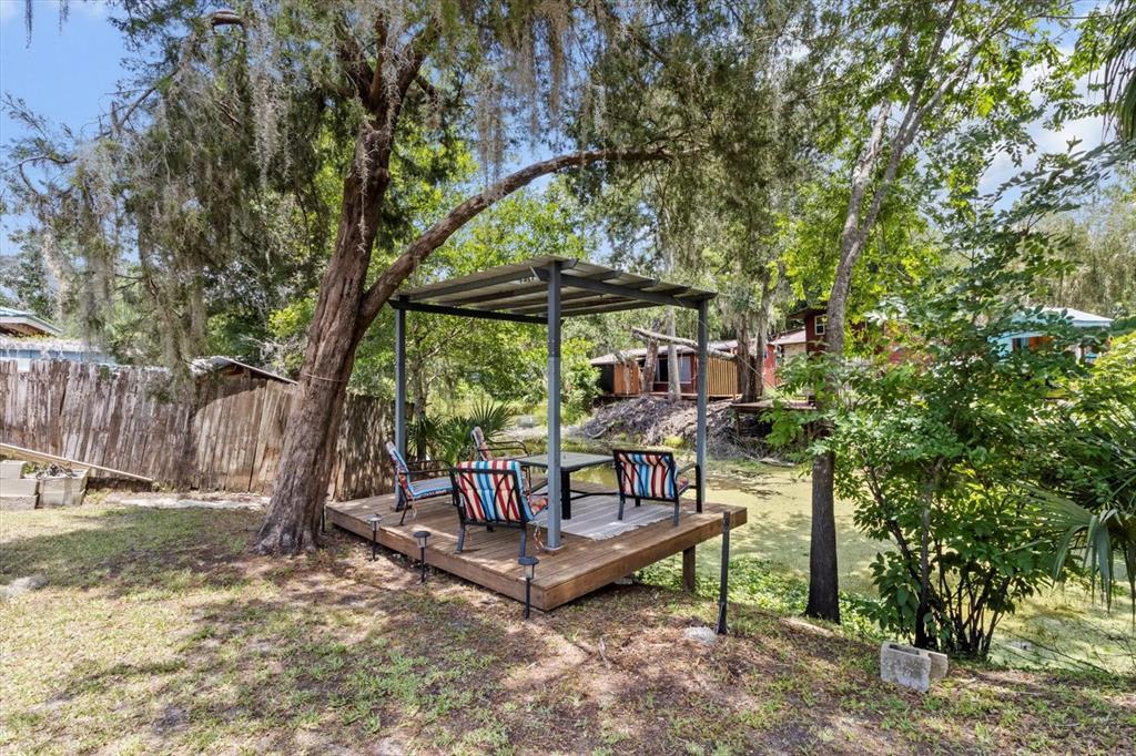 A wooden deck with a metal-roofed pergola and outdoor seating sits beside a pond — 609 S REDBUD TERRACE, INVERNESS, FL