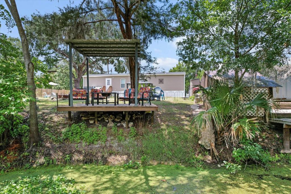 A wooden deck with a metal pergola overlooks a pond behind a residential property — 609 S REDBUD TERRACE, INVERNESS, FL