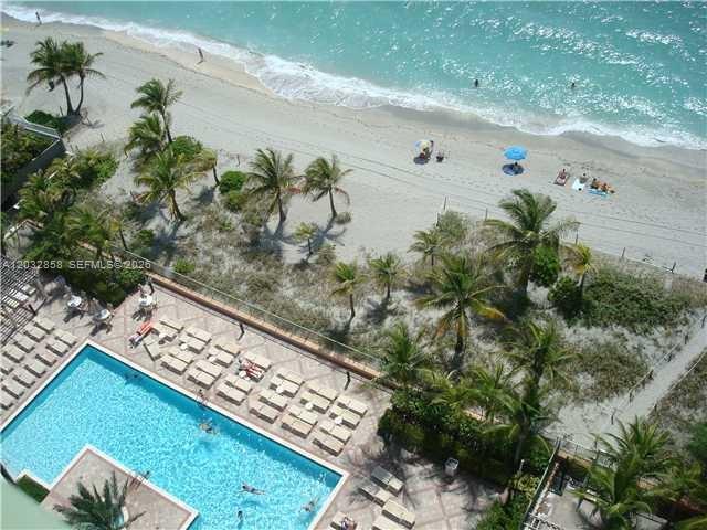 An aerial view shows a swimming pool with lounge chairs next to a sandy beach — 2080 S Ocean Dr # 1512, Hallandale Beach FL 33009, HALLANDALE BEACH, FL