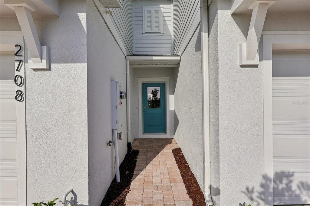 A paved walkway leads to a blue front door nestled between two white garage walls — 2708 MEADOW CREST DRIVE, ST CLOUD, FL