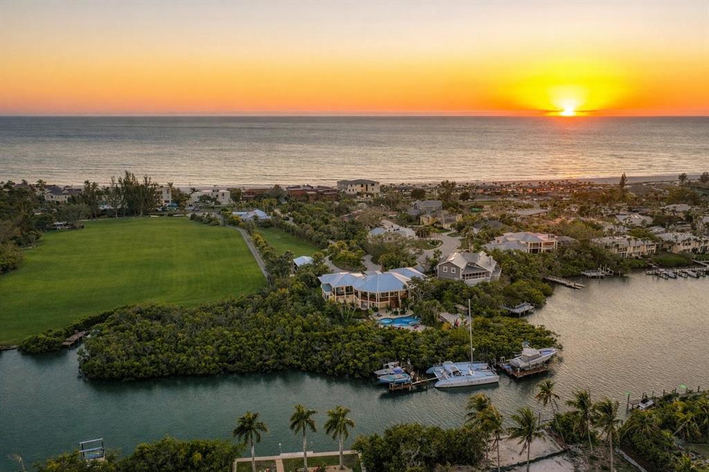 An aerial view shows a waterfront house with a pool surrounded by trees at sunset — 6680 GULF OF MEXICO DRIVE, LONGBOAT KEY, FL