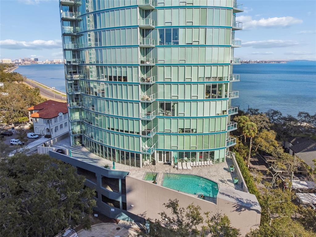 An aerial view shows a curved glass high-rise building with a pool deck and waterfront — 2900 W BAY TO BAY BOULEVARD UNIT 501, TAMPA, FL