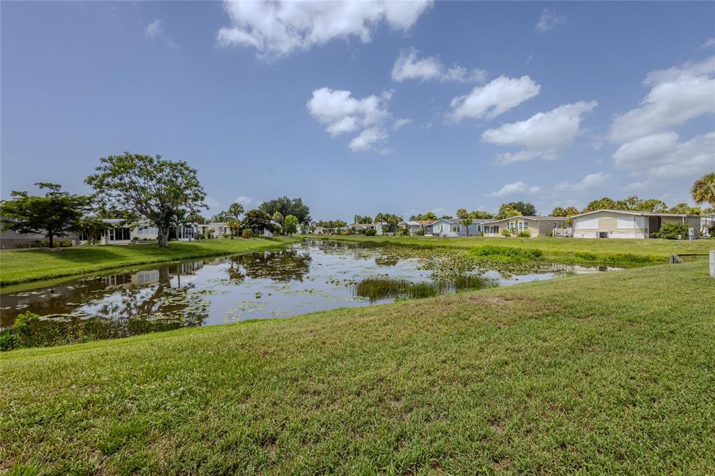 A grassy lawn slopes down to a pond surrounded by houses under a blue sky — 2100 KINGS HIGHWAY UNIT 274, PORT CHARLOTTE, FL