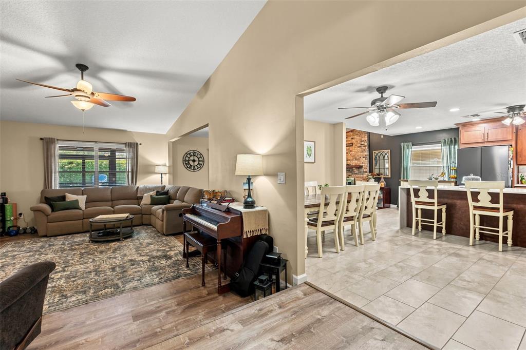 An open-concept living room with a sectional sofa, piano, and adjacent dining area and kitchen — 8736 LARWIN LANE, ORLANDO, FL