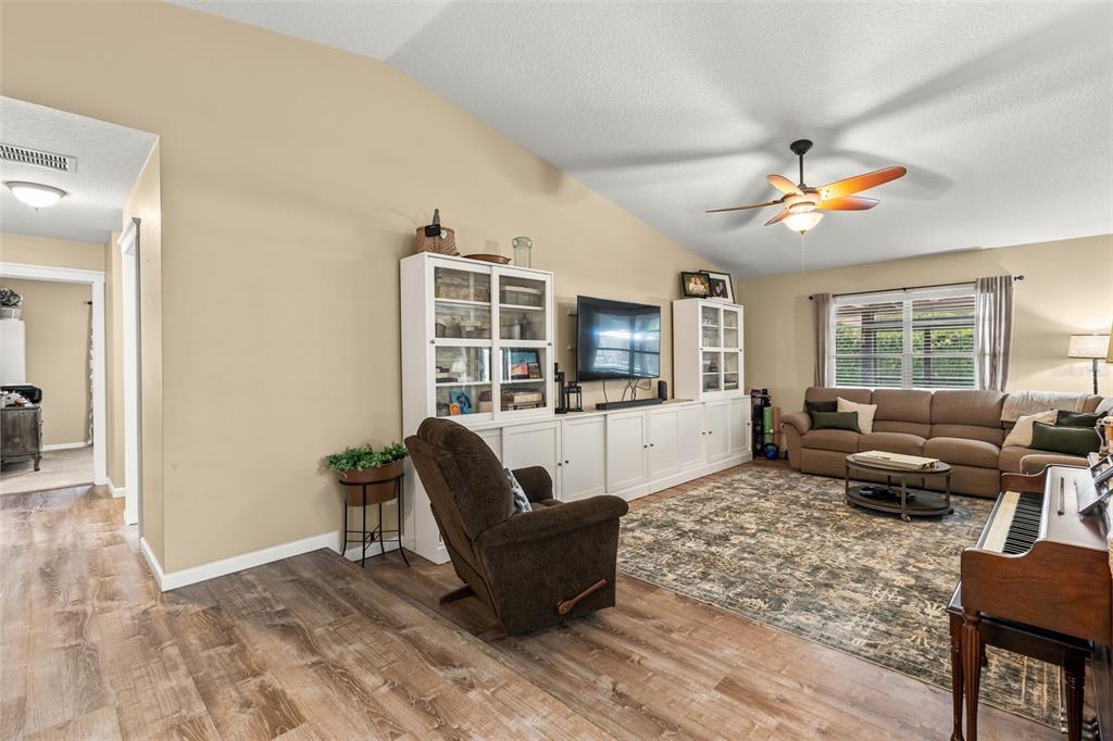 A living room features a vaulted ceiling, wood-look flooring, built-in white cabinetry, and a sectional — 8736 LARWIN LANE, ORLANDO, FL