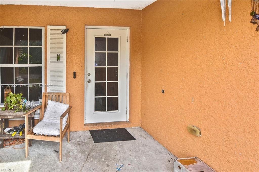 A wooden chair with a white cushion sits on a concrete porch beside a door — 2612 66 st w, Lehigh Acres FL 33971, LEHIGH ACRES, FL